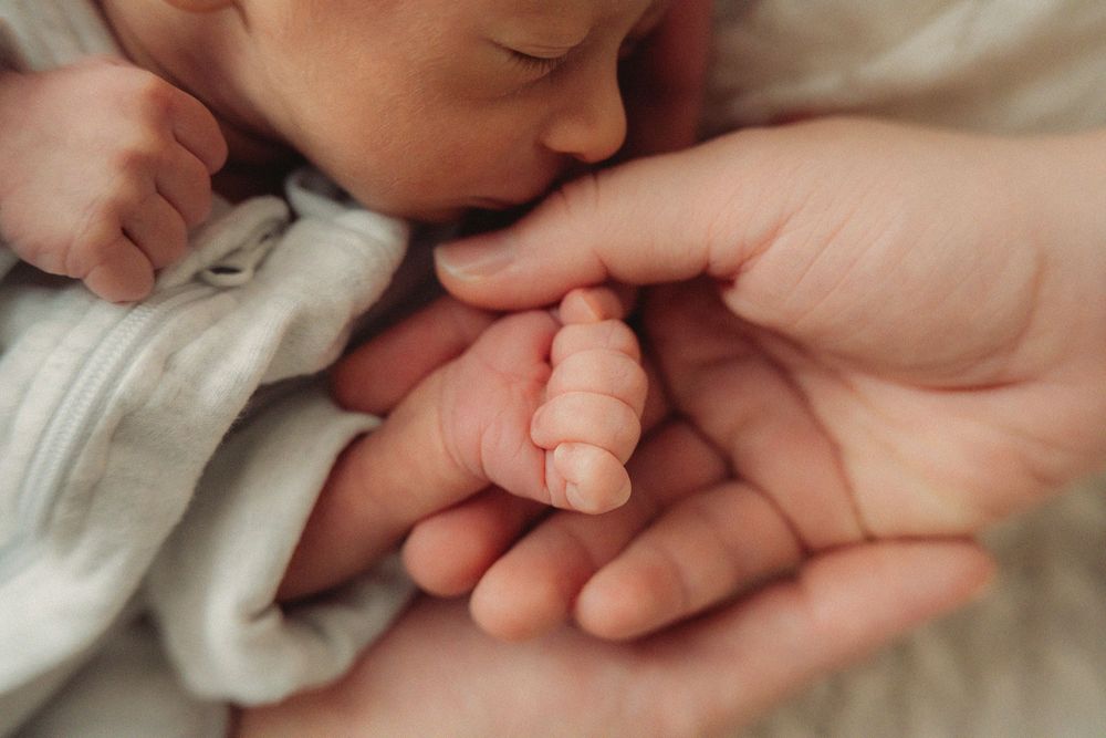 Tender close-up of tiny newborn hand being held by parent.