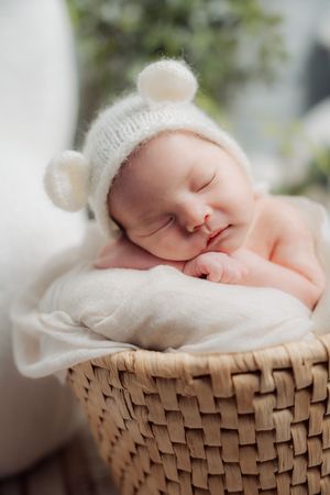 Sleeping newborn wrapped in white blanket resting peacefully in woven basket.