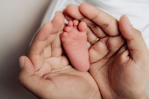 Gentle hands cradling tiny newborn feet against white background.