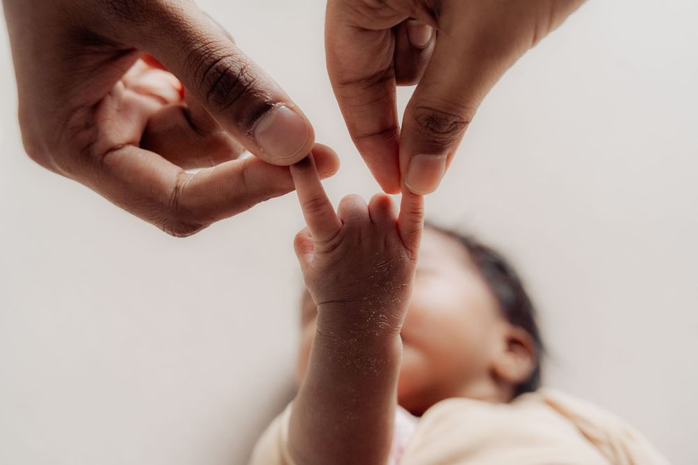 Close-up of tender hands reaching towards sleeping newborn in soft lighting.