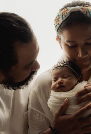 Tender moment of parents holding their sleeping newborn in soft natural light.