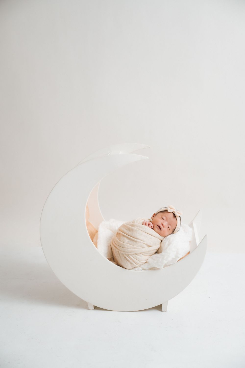 Creative newborn photography with baby sleeping in white curved prop on light background.