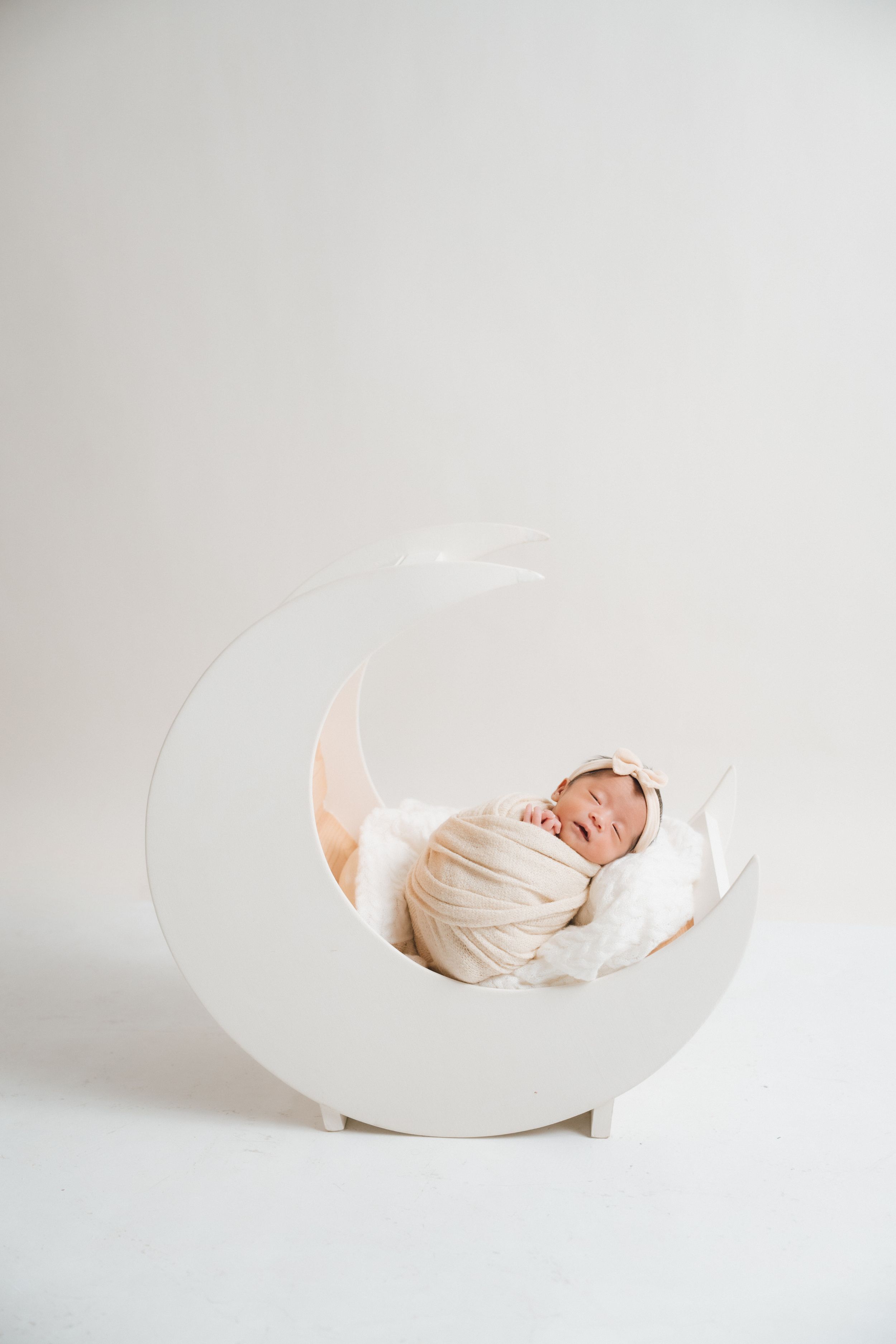 Creative newborn photography with baby sleeping in white curved prop on light background.