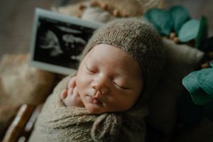 Intimate newborn photography session with baby wrapped in cozy green blanket.