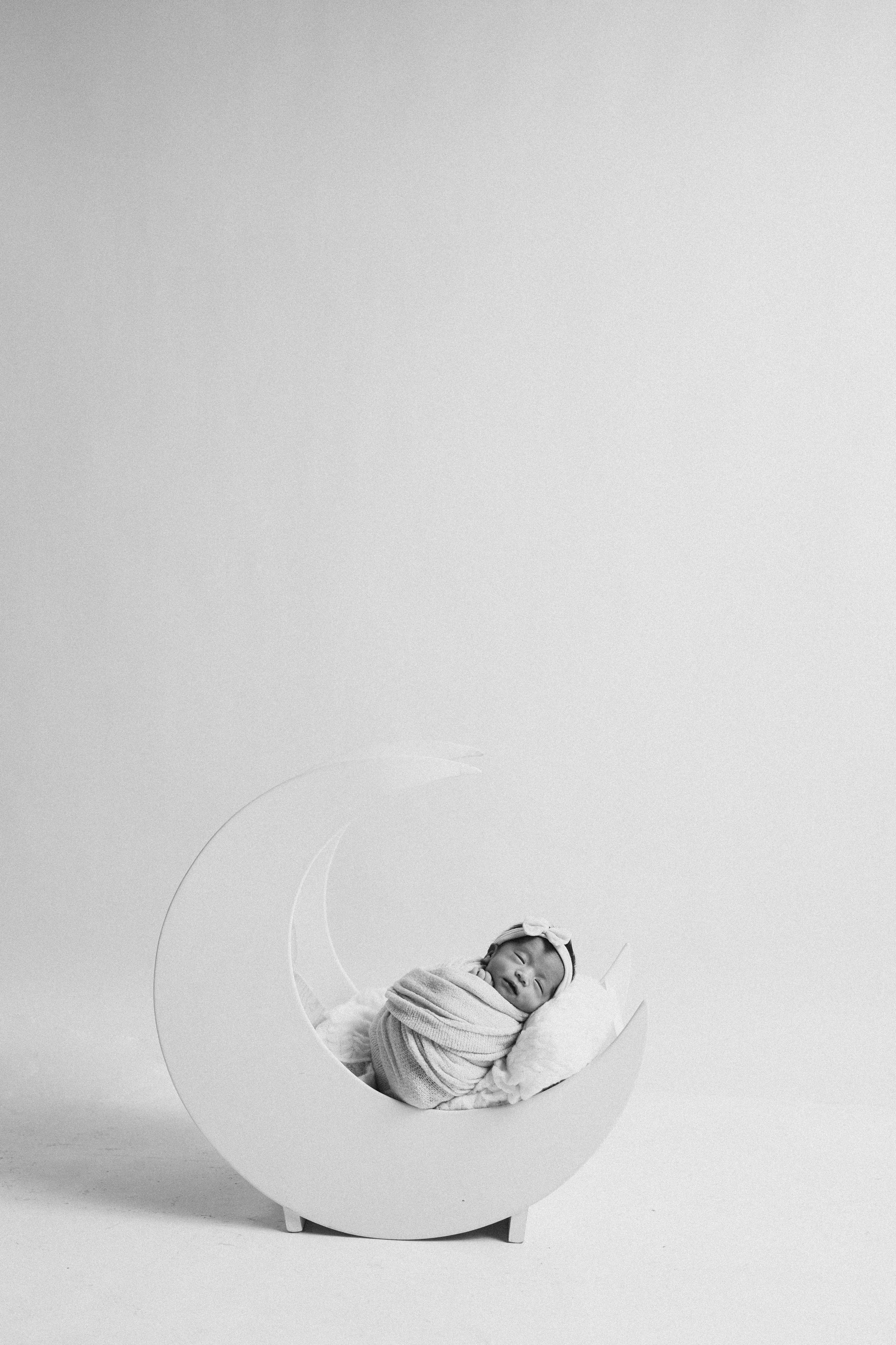 Artistic black and white portrait of sleeping newborn in curved white prop.