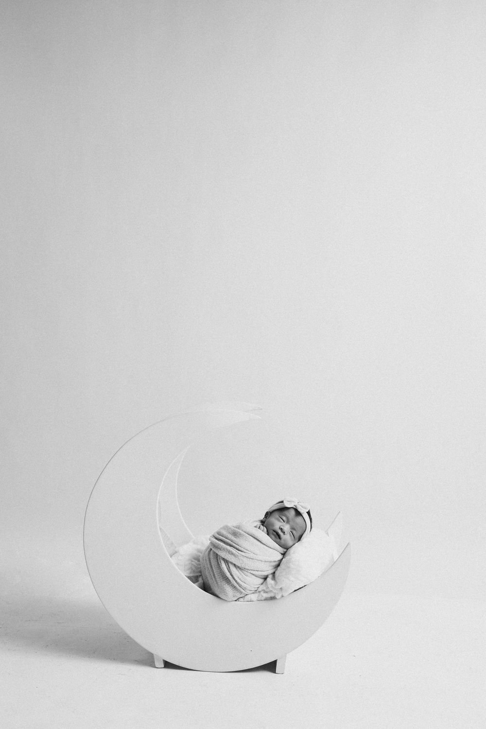 Artistic black and white portrait of sleeping newborn in curved white prop.