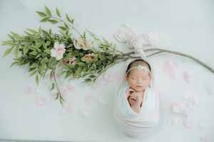 Sleeping newborn wrapped in white swaddle with floral and greenery decoration.