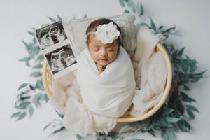 Serene newborn photography setup with soft white wrapping and eucalyptus leaf accents.