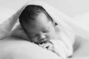 Peaceful sleeping newborn wrapped in white blanket against light background.