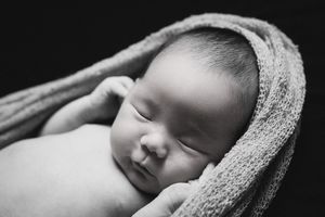Peaceful sleeping newborn baby wrapped in soft gray blanket in black and white portrait.