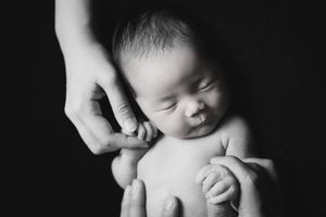 Close-up black and white portrait of sleeping newborn with supporting hands.