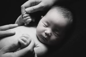 Artistic black and white photo of sleeping infant with hands gently supporting.