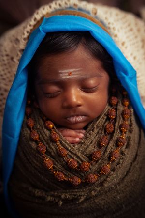 Newborn wrapped in blue and brown textured fabrics with decorative elements.