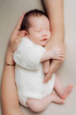 Sleeping newborn wrapped in soft white blanket nestled in caring arms.