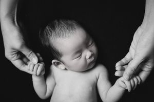 Minimalist black and white portrait of sleeping newborn supported by caring hands.