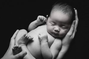 Tender black and white portrait of newborn baby cradled in protective hands.