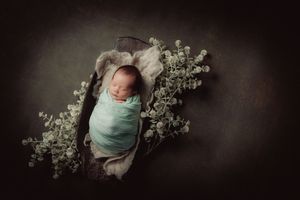 Peaceful newborn sleeping surrounded by delicate white flowers in dark moody setting.