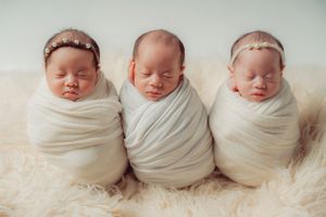 Triplet of newborn babies wearing white wraps and delicate headbands.