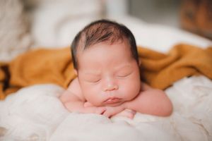Peaceful sleeping newborn on soft white blanket with orange accent.