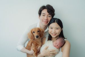 Lifestyle family photo with golden retriever and newborn baby against white wall.