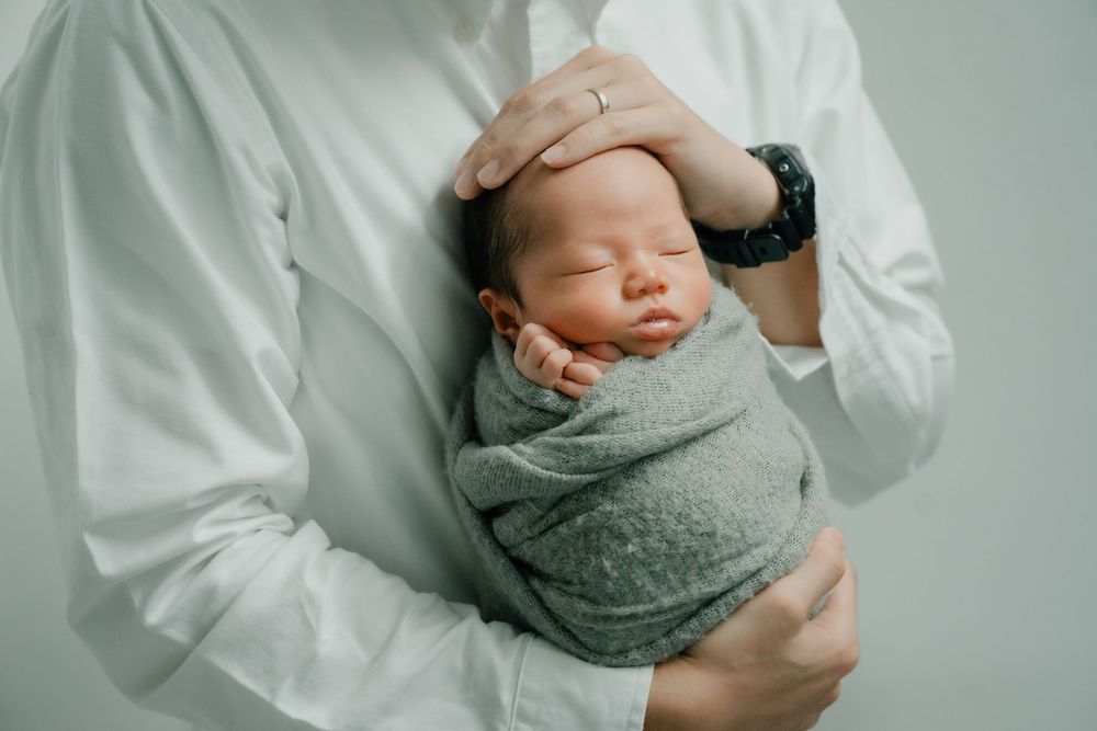 Gentle family portraits showing parents cradling newborn wrapped in grey fabric.