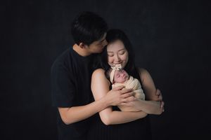 An intimate family moment captured against a dark backdrop as parents embrace their newborn.