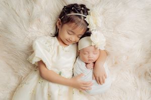 Sleeping newborn baby wrapped in white fabric on soft cream fur backdrop.