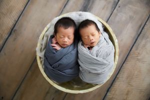 Twin newborns sleeping peacefully together in gray swaddles on wooden background.