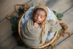 Baby sleeping peacefully in wooden basket with soft textured wraps.