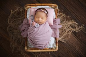 Baby resting in wooden basket with pink wrap and rustic wooden background.