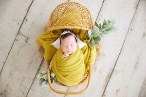 Newborn photography setup with mustard yellow wrap and greenery on white wooden floor.