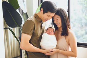 New parents sharing a tender moment with their newborn baby near a window.