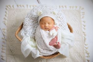 Baby sleeping in basket with white lace details and delicate bow accessories.