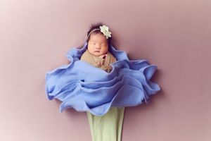 A sleeping newborn wrapped in flowing blue fabric styled as a flower.