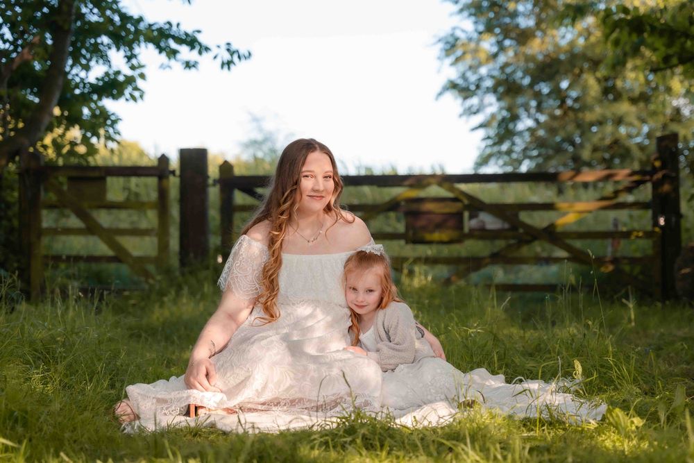 Mother and daughter share tender moments in a sunlit meadow wearing matching white lace dresses.
