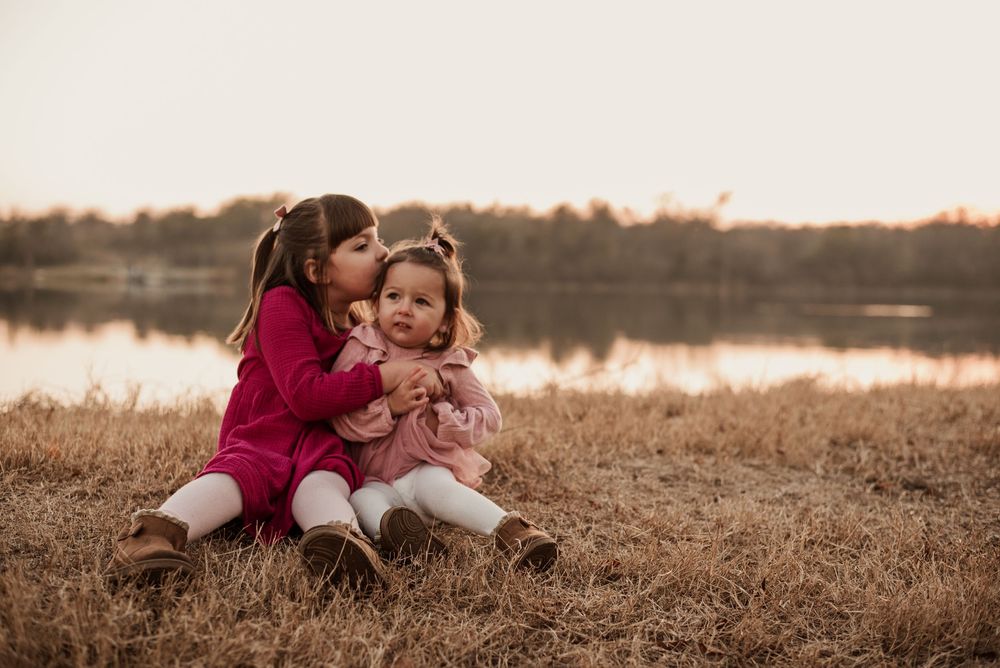 A loving moment captured between two figures sitting in a golden field at sunset by a lake.