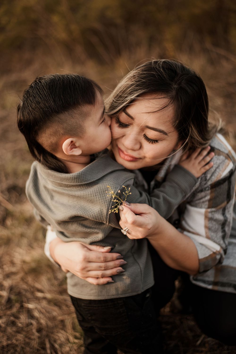 A tender moment captured outdoors as a child gives a sweet kiss while holding small wildflowers.