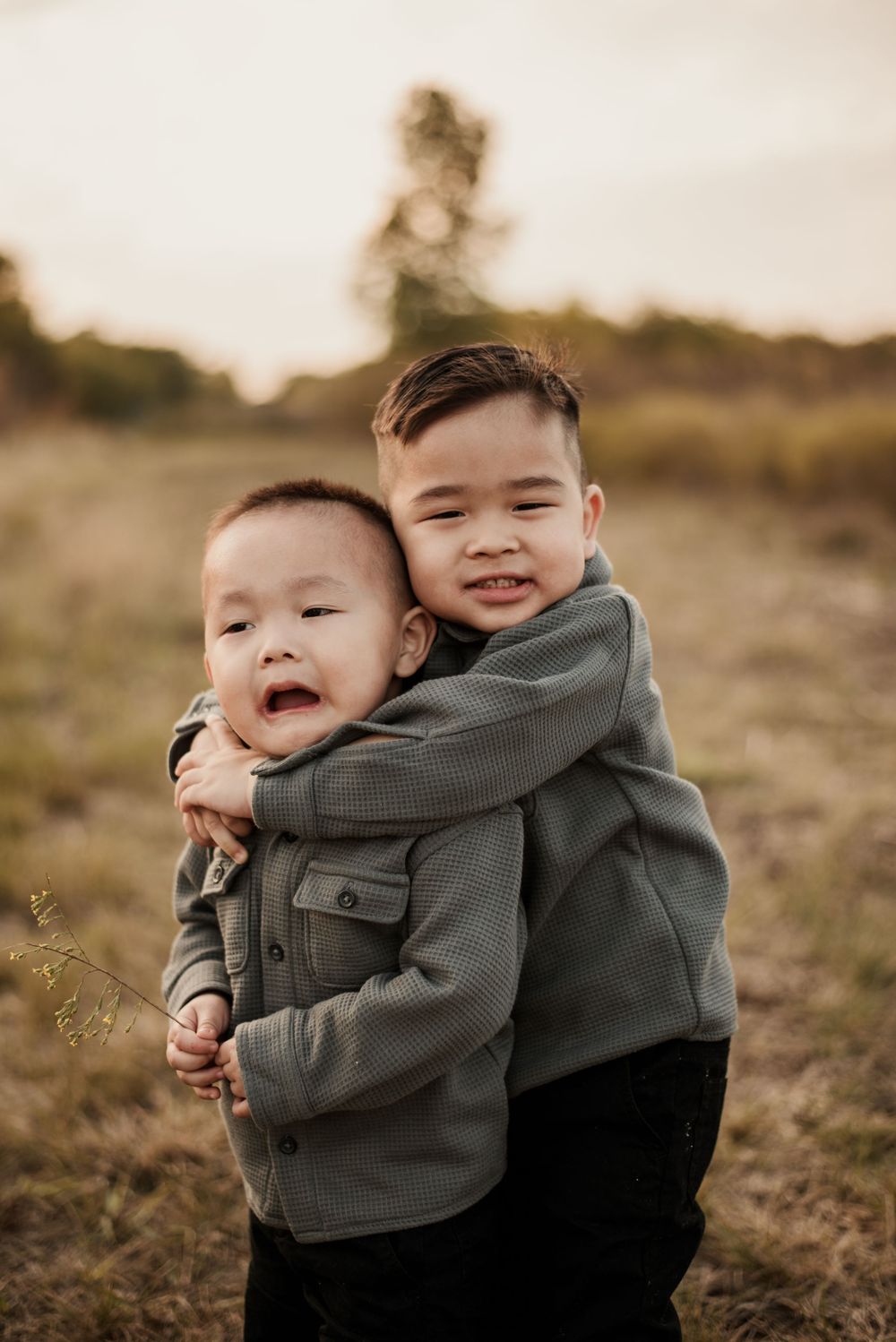 Two children share a joyful embrace while playing outdoors during golden hour.
