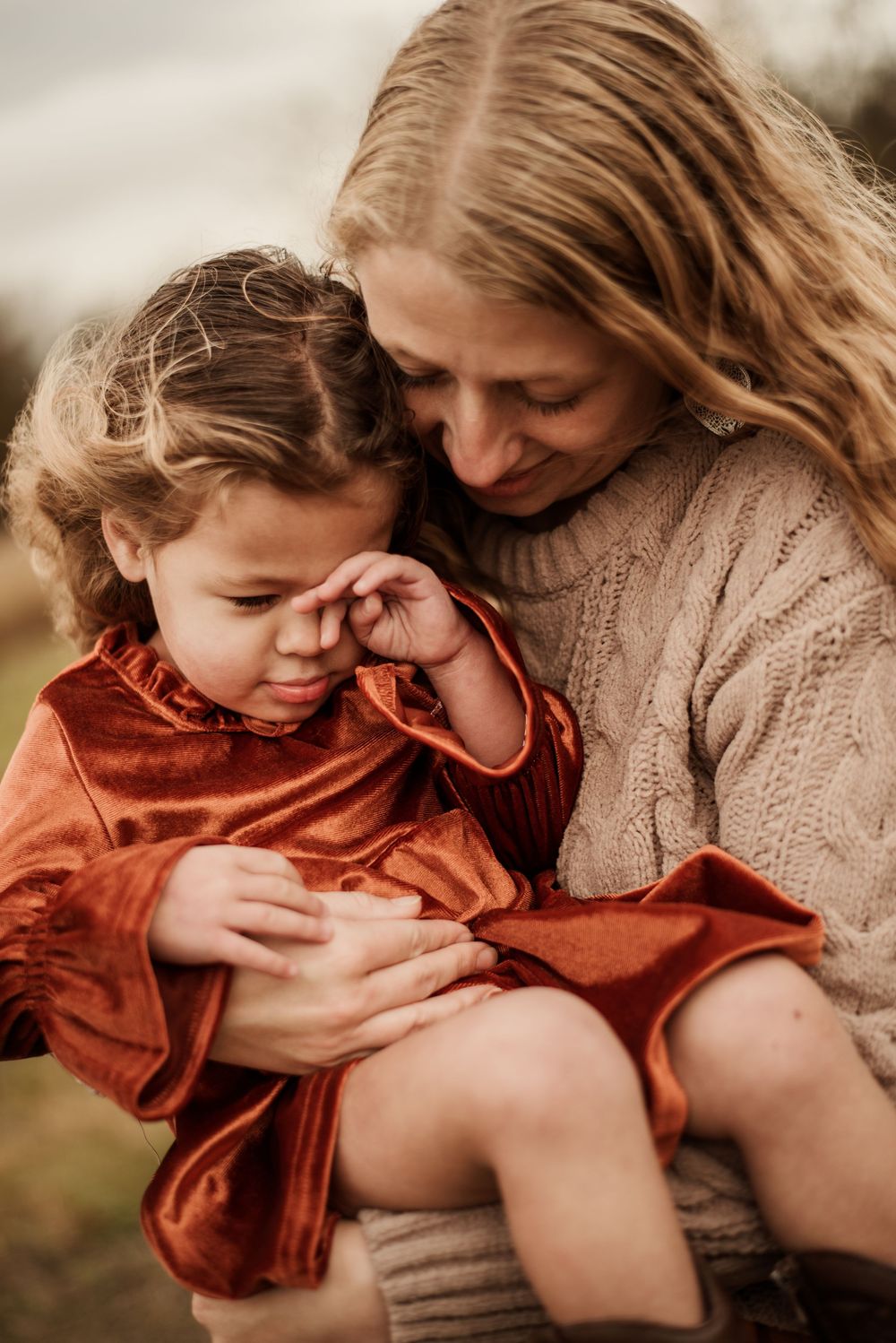 A tender moment between parent and child wearing cozy sweaters in warm earth tones during an outdoor photoshoot.