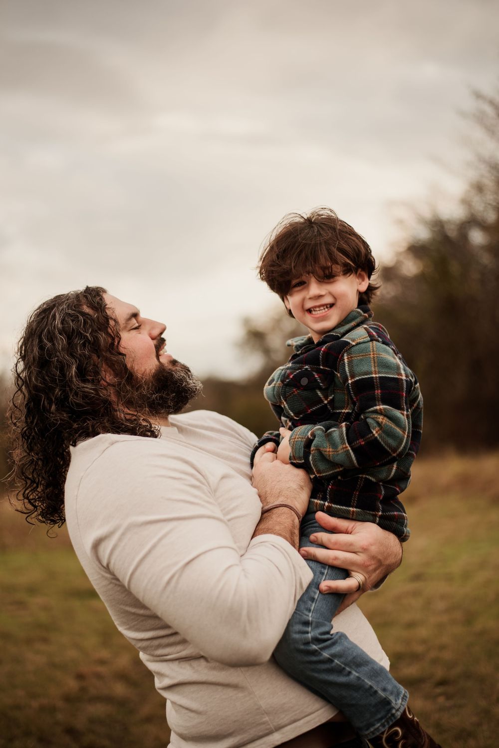 A parent and child share joyful moments together while playing outdoors in a field on an overcast day.