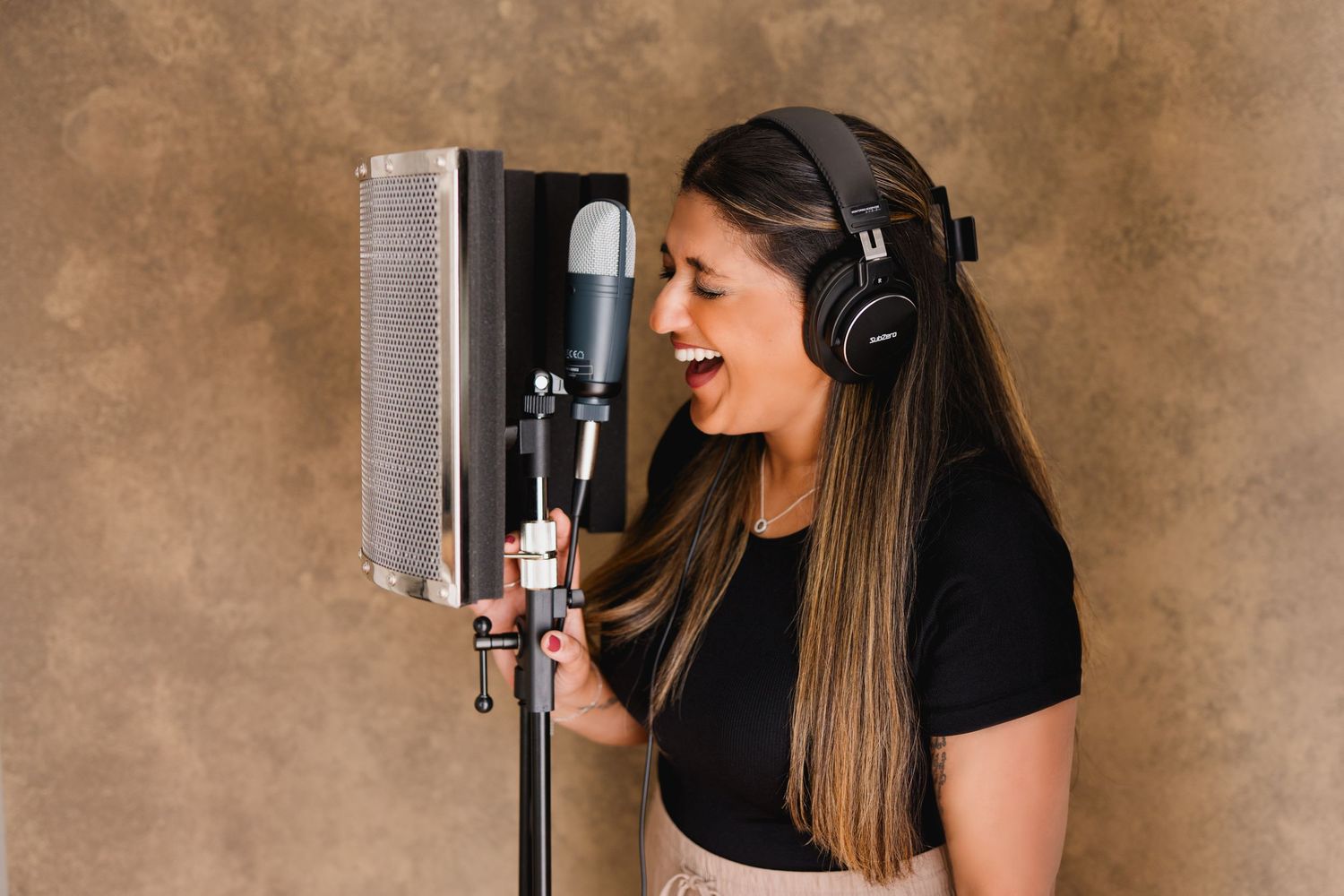 Singer recording vocals in a studio with headphones and microphone with a pop filter against a brown background.