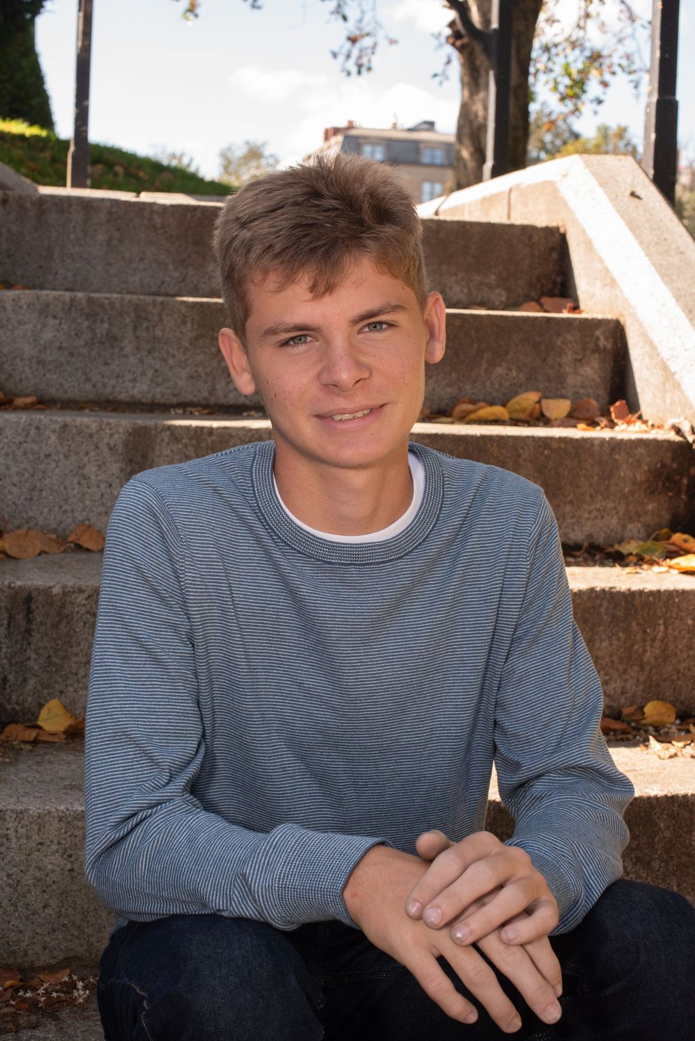 A youth in a gray sweatshirt sits outdoors on stone steps during autumn.