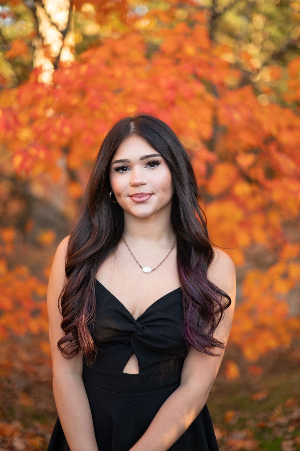 Portrait of someone in a black dress against vibrant orange autumn foliage in the background.