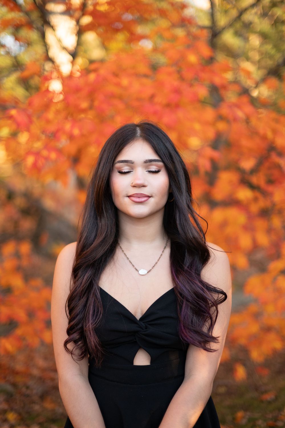 Close-up portrait with closed eyes against a backdrop of bright orange fall leaves.
