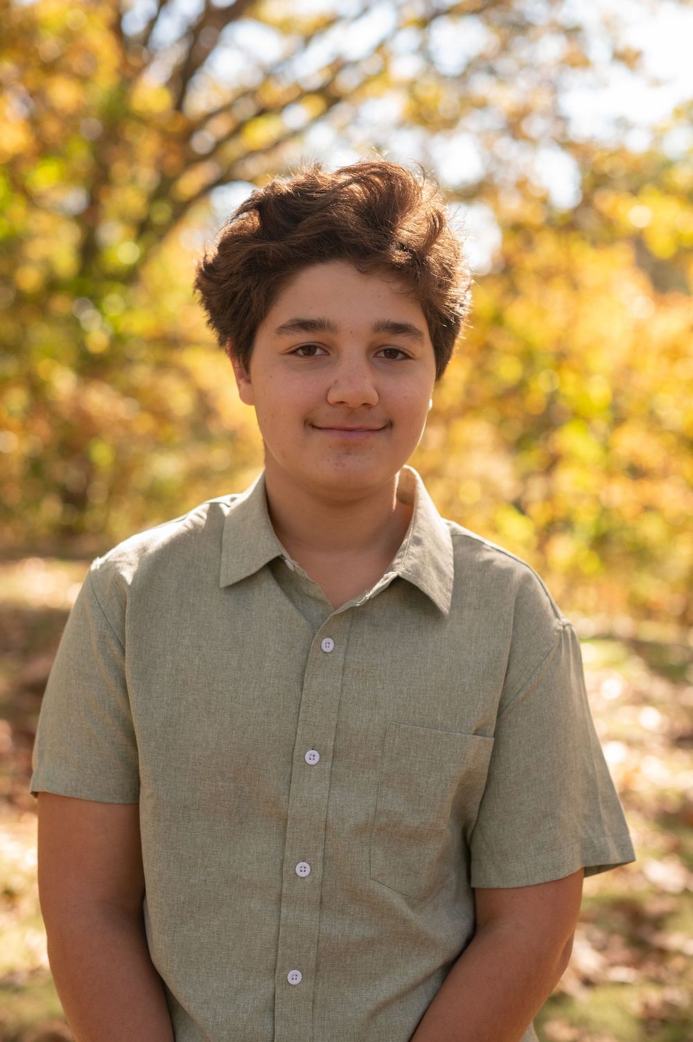 Someone wearing a light colored polo shirt poses outdoors with fall foliage creating a warm golden backdrop.