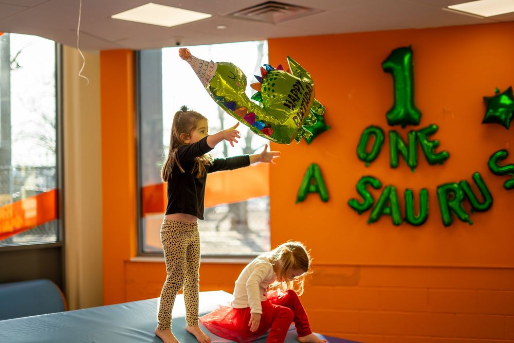 Children participate in a dance class with green decorations on an orange wall in a bright studio space.