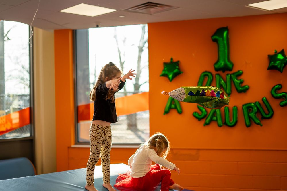 Children playing in a bright orange room with green decorative wall art and numbers.