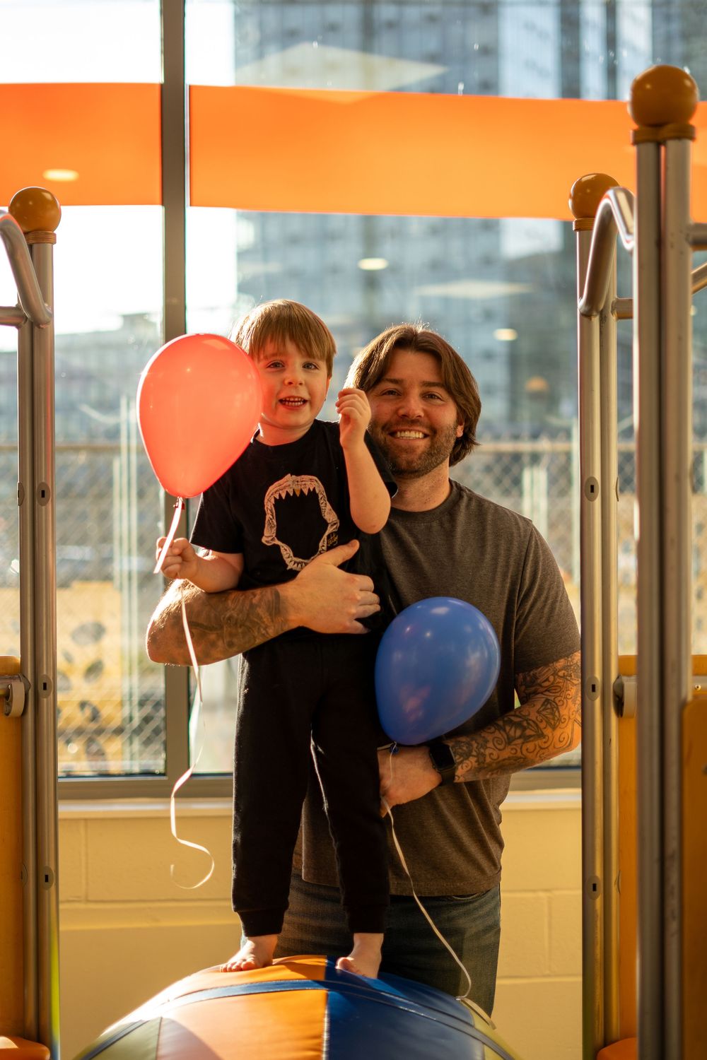 People holding colorful balloons gather in a modern office space with large windows and orange accents.