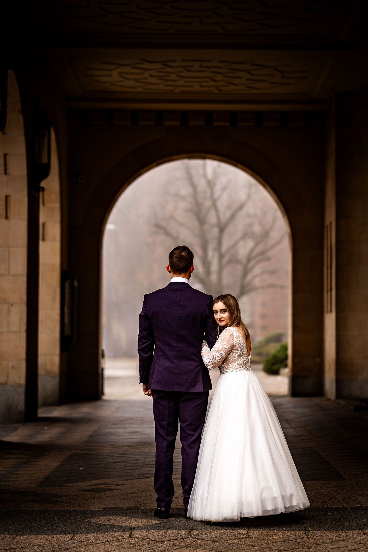 A wedding couple stands in silhouette under an ornate stone passageway.