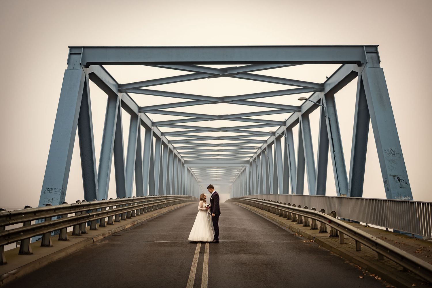 A wedding couple stands in the center of a geometric steel bridge structure.